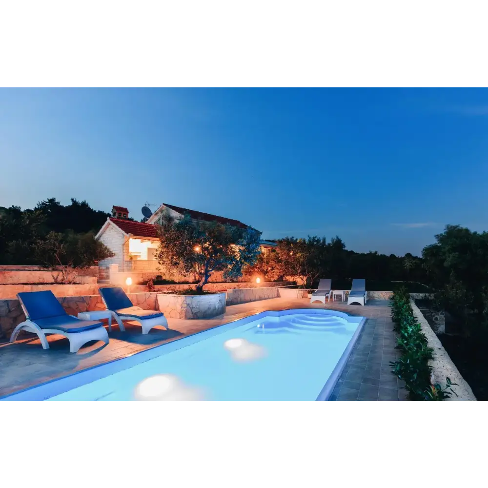 Blåvita loungestolar vid lysande Haiti trädgårdspool med avrundad trappa vid skymning